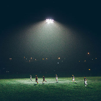 Spotlight on a football pitch at night with teams playing