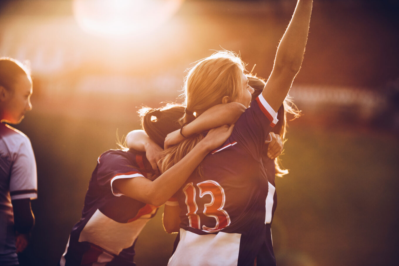Team of happy female football players celebrating their achievement on a playing field at sunset.
