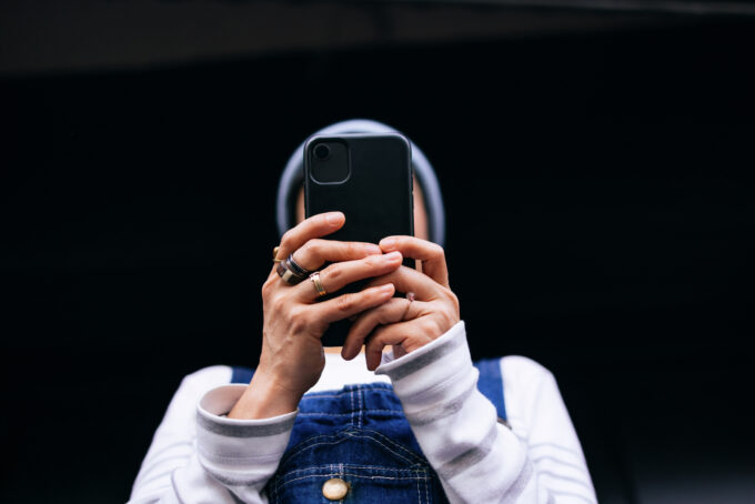 Low angle view of a person typing on their smartphone while standing in front of black wall.